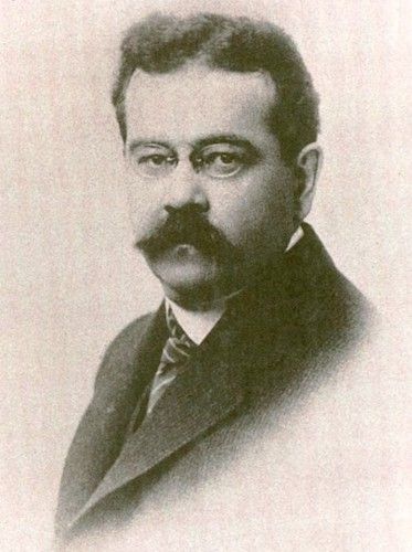 sepia photograph of a round-faced man with spectacles and a big mustache