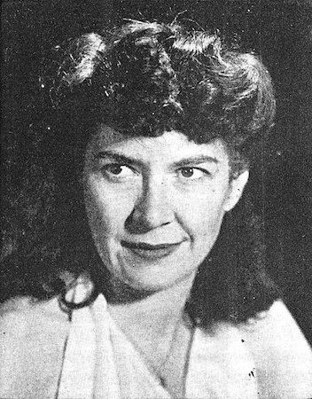 Black and white photograph of a dark-haired woman with a mullet-type hairstyle, dark lipstick and a white halter top dress. She looks kind of fey and mysterious but perhaps I'm just projecting.