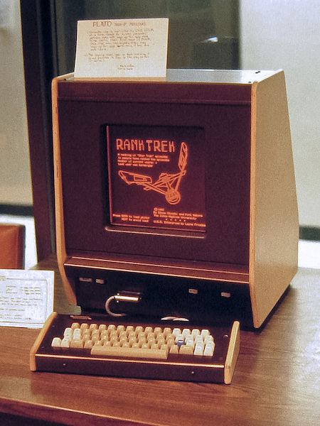 An early computer terminal with gorgeous brown and beige finish, a ticky-tacky looking keyboard, and a narrow monitor that displays in two colours (brown and orange). The display shows the start screen of a game called 'Rank Trek' with an image of the Starship Enterprise.