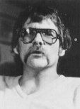 Black and white photo of a man with a huge handlebar moustache, aviator sunglasses, and a choppy haircut.