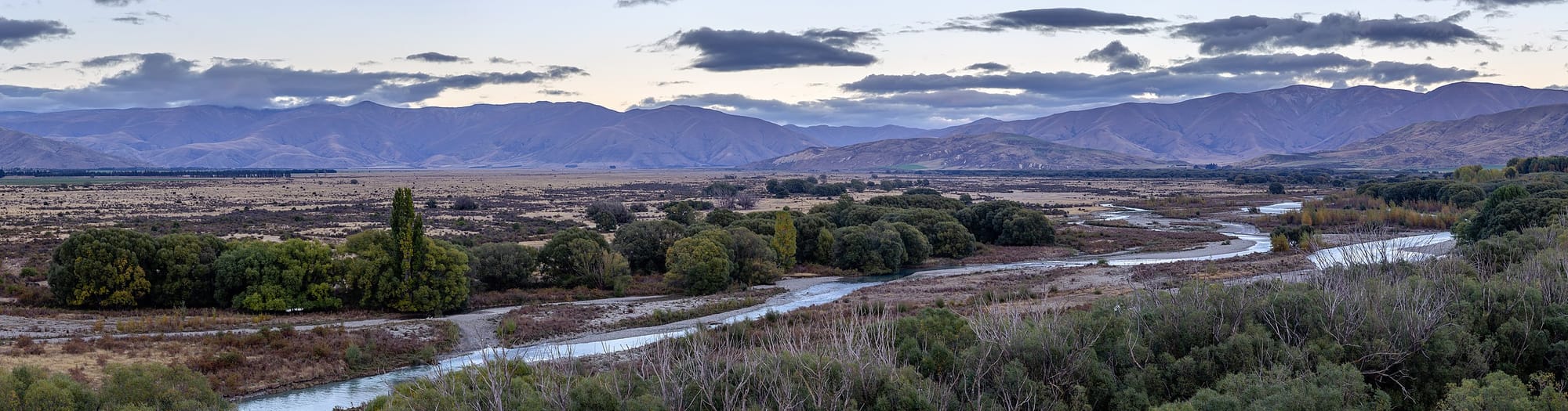 a narrow river winds through a flat plain, with mountains all across the distant horizon.