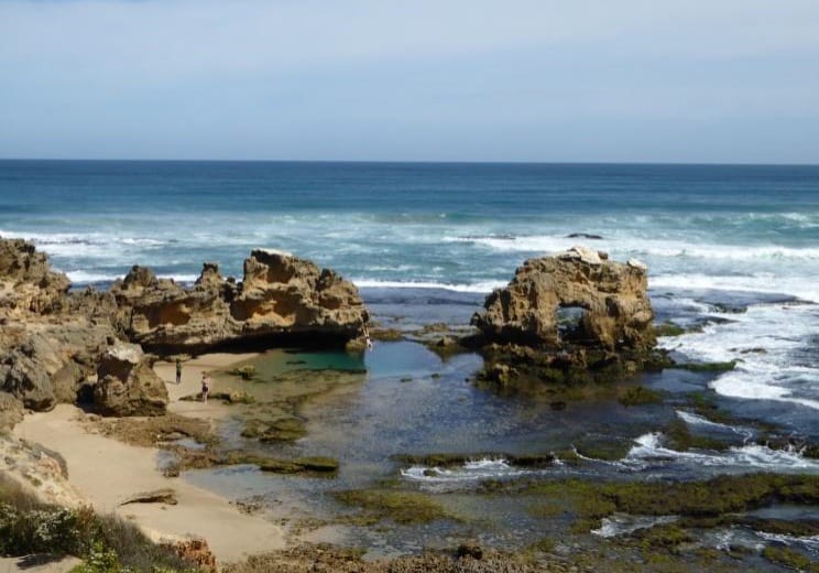 A beach scene with sheltered rockpools and gnarled-looking pillars of stone.