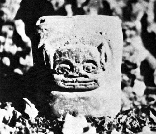 Stone statuette with a goblinoid face carved into a square block. It is photographed in grainy black and white, giving the whole image an air of a lost document, very much like something from a Lovecraft story